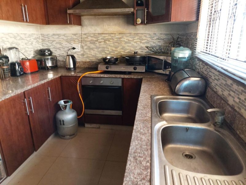 A functional kitchen featuring dark wood cabinetry, granite countertops, a double stainless steel sink, and a built-in oven with a gas hob.