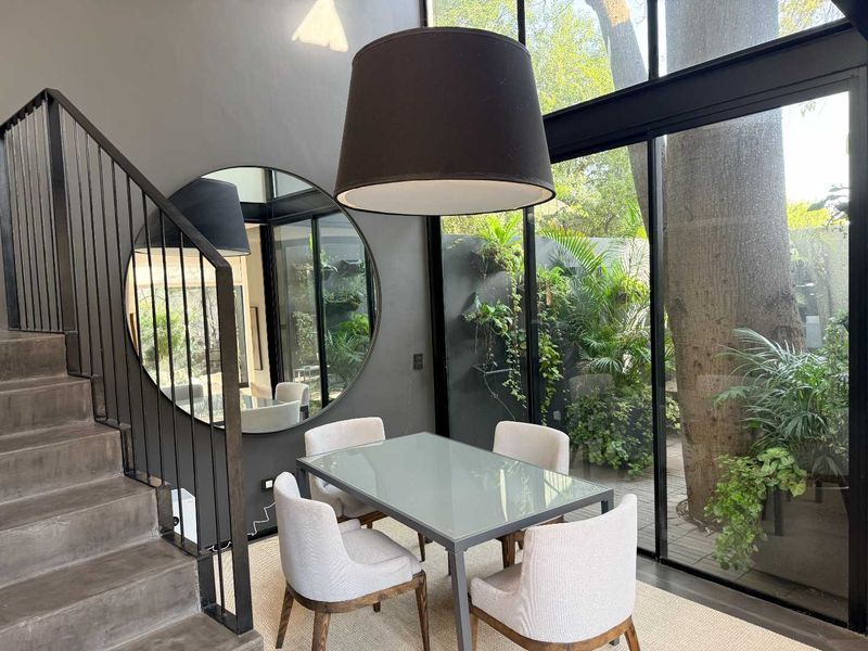 Modern dining area featuring a sleek staircase, dark feature walls, and expansive floor-to-ceiling windows overlooking a lush private garden.