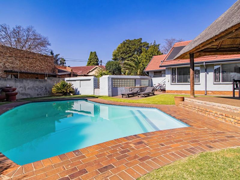 Outdoor pool area featuring a swimming pool, brick paved surround, and a covered thatched lapa, set within a private garden with boundary walls.
