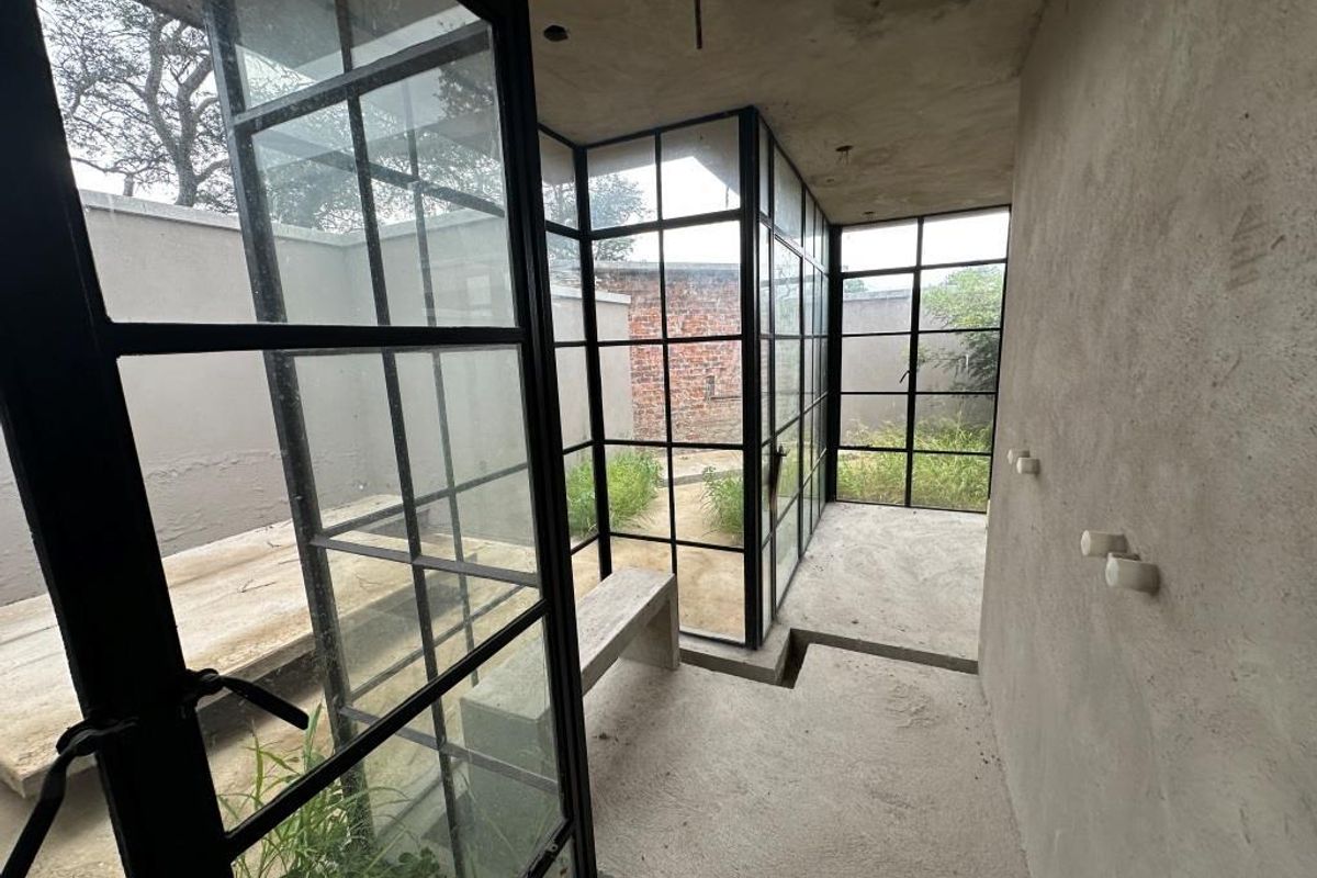 An unfinished interior space featuring industrial-style black steel-framed glass walls and concrete flooring, offering a raw, modern architectural aesthetic.