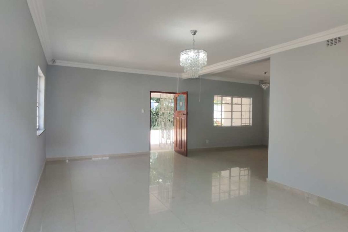 Spacious, light-filled living area featuring neutral wall tones, polished tiled flooring, and elegant crystal chandelier lighting, offering a versatile open-plan layout.