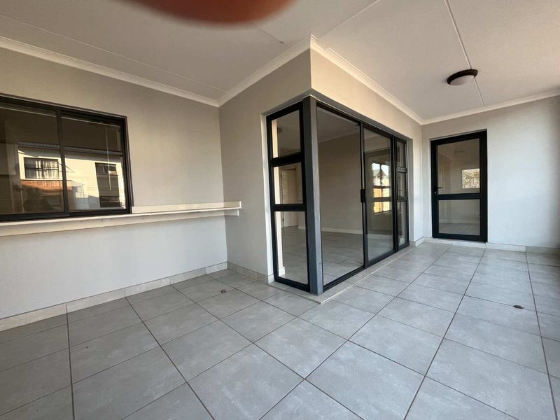 A clean, covered patio area featuring neutral floor tiles, modern aluminium-framed sliding doors, and a fixed shelf, offering a versatile outdoor living space.