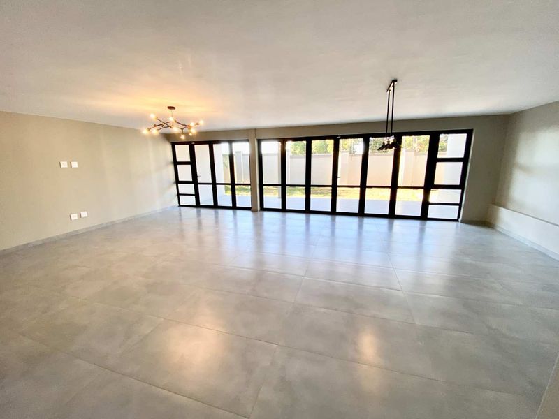 Spacious, light-filled living area featuring large-format floor tiles and expansive black-framed folding glass doors that open to the exterior.