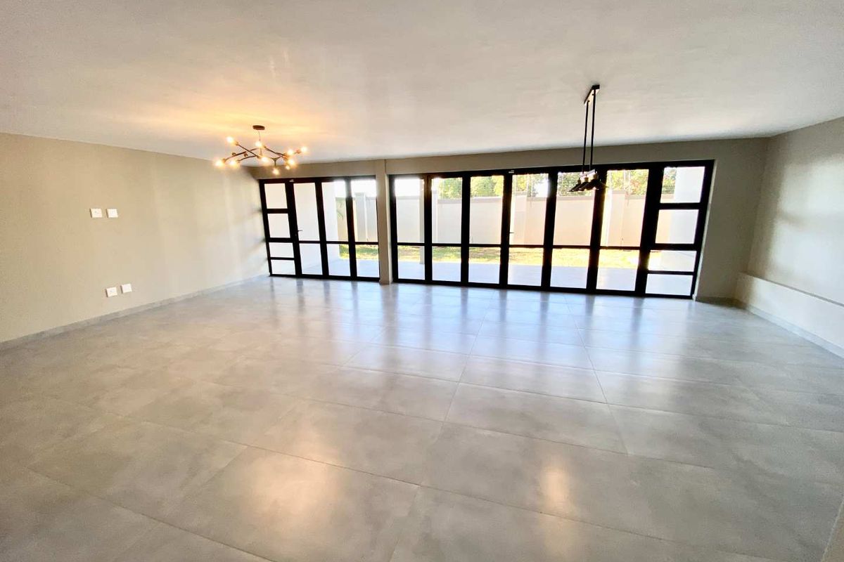Spacious, light-filled living area featuring large-format floor tiles and expansive black-framed folding glass doors that open to the exterior.
