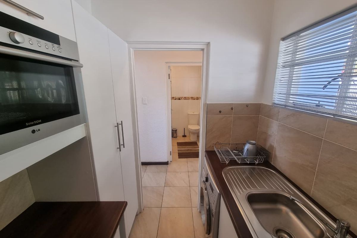 Compact kitchen featuring built-in cabinetry, integrated microwave, stainless steel sink, and tiled splashbacks, with a direct view into an adjacent bathroom.