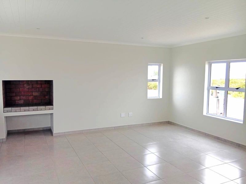 A bright, empty living room featuring tiled floors, a built-in brick fireplace, and large windows providing natural light.