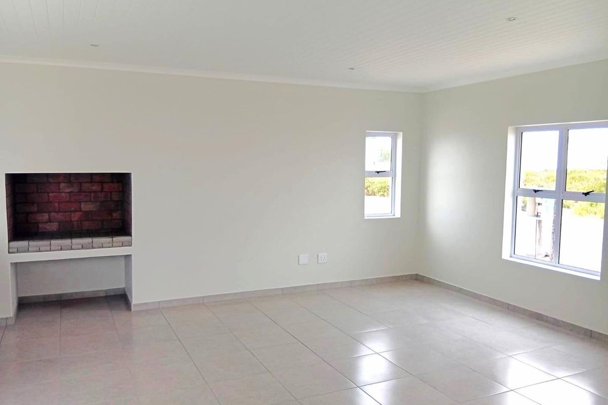 A bright, empty living room featuring tiled floors, a built-in brick fireplace, and large windows providing natural light.