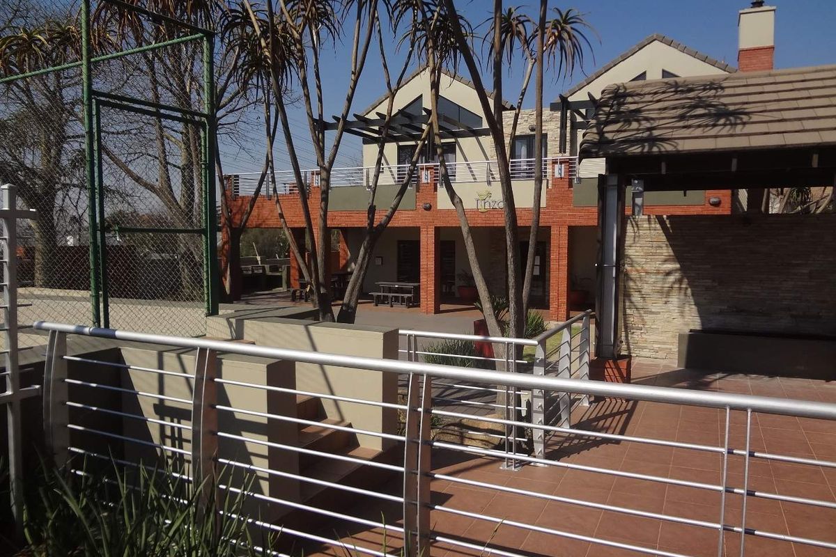 Rear view of the apartment complex featuring a tiled patio area, stainless steel balustrades, brick facade, and a pergola structure.