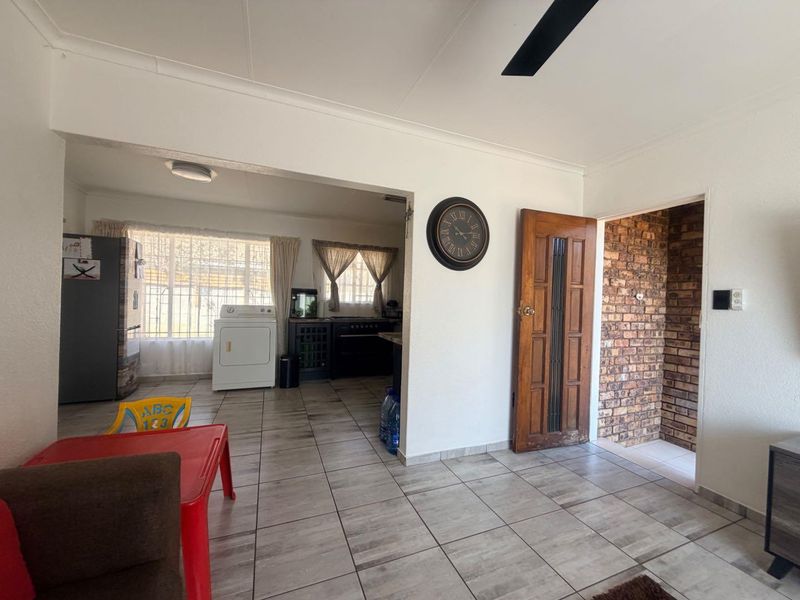 Open plan living area featuring tiled flooring, an exposed brick accent wall, and a ceiling fan, connecting to a kitchen and laundry space.