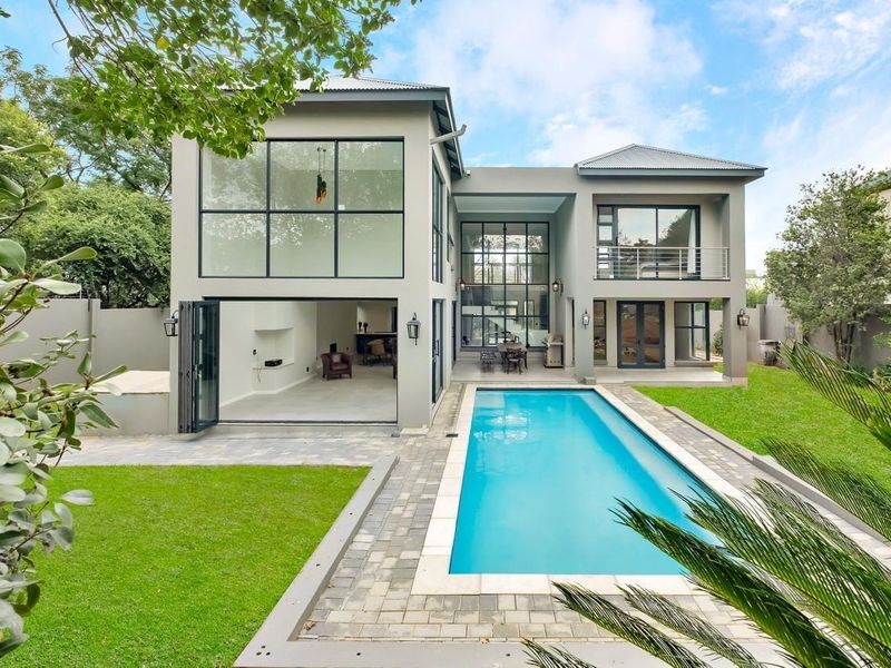 Rear view of a modern cluster home featuring a swimming pool, landscaped garden, large glass windows, and a balcony.