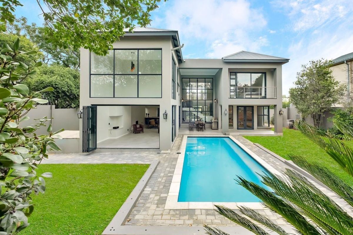 Rear view of a modern cluster home featuring a swimming pool, landscaped garden, large glass windows, and a balcony.