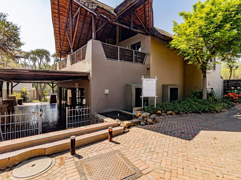 Exterior view of a property featuring a thatched roof, timber decking, and a paved driveway entrance with a small water feature.