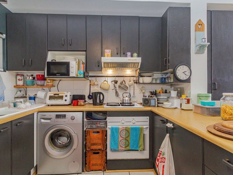 A functional kitchen featuring dark cabinetry, light wood-look countertops, a tiled backsplash, and integrated appliances including an oven, hob, and washing machine.