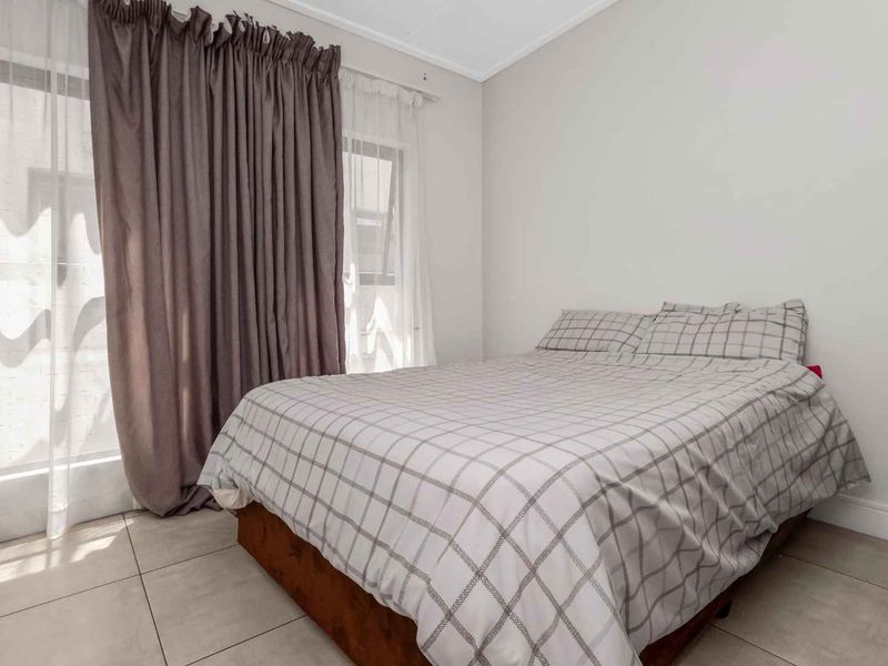 A well-lit bedroom featuring neutral tiled flooring and a sliding glass door with curtains, providing access to the exterior.