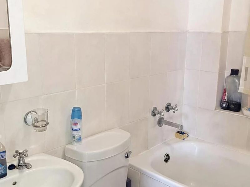 A functional bathroom featuring a pedestal sink, standard toilet, and a bathtub with wall-mounted fixtures and tiled wall surrounds.