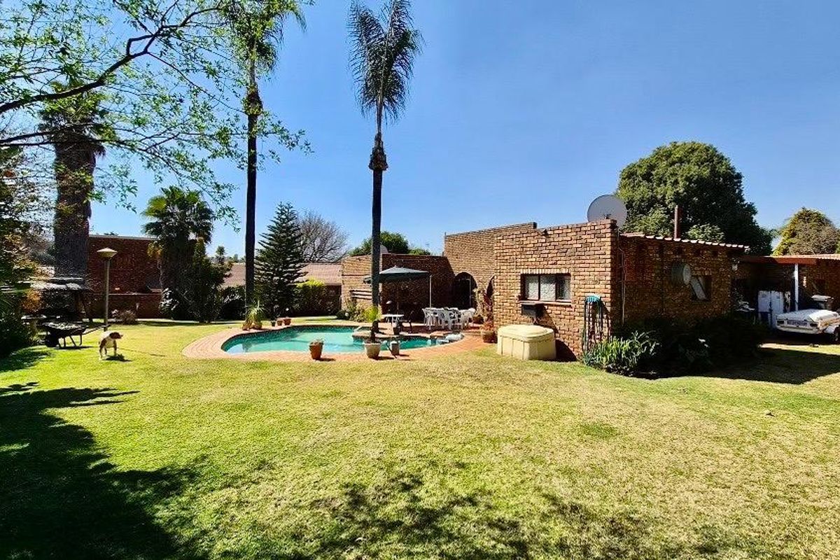Spacious rear garden featuring a swimming pool with paved surround, established trees, and a brick-faced house exterior.