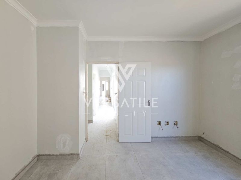 An empty bedroom featuring tiled flooring and coved ceilings, currently undergoing finishing work with exposed wiring and incomplete wall surfaces.