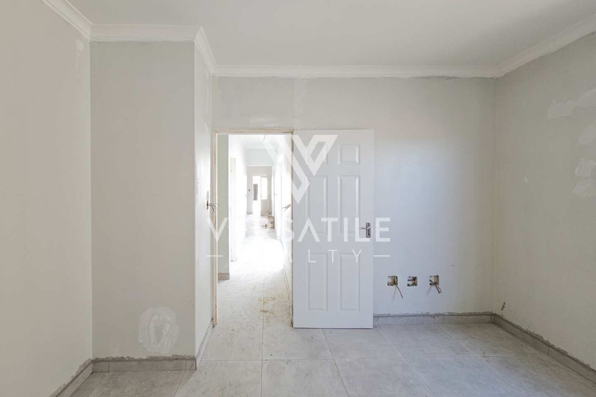 An empty bedroom featuring tiled flooring and coved ceilings, currently undergoing finishing work with exposed wiring and incomplete wall surfaces.