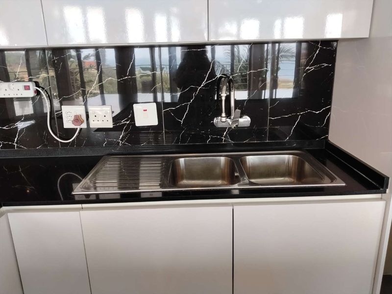 Modern kitchen area featuring white gloss cabinetry, a black stone countertop, and a striking black marble-look splashback with a double bowl stainless steel sink.
