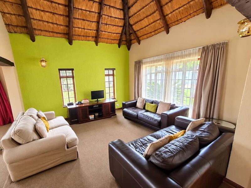 Spacious living room featuring a high vaulted thatched ceiling with exposed timber beams and large windows providing natural light.