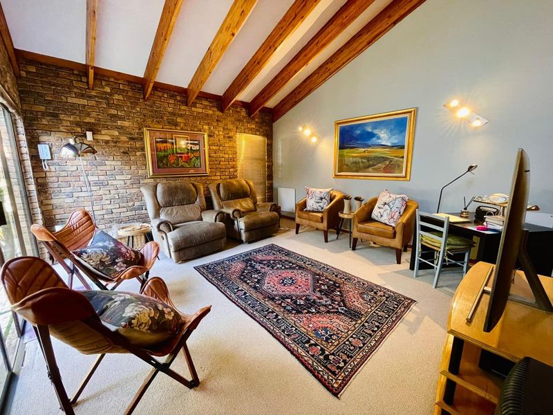 Spacious living room featuring a vaulted ceiling with exposed timber beams and a rustic brick feature wall, complemented by large sliding glass doors.