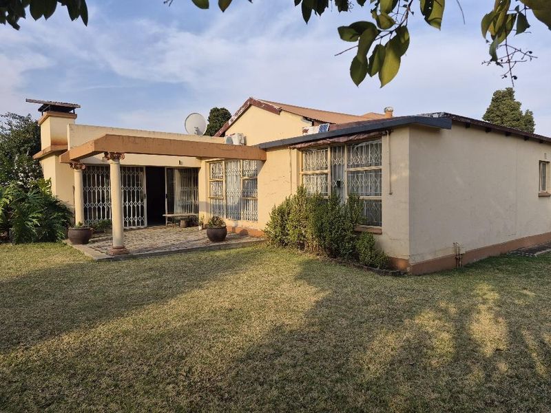 Rear view of the house featuring a covered patio, security gates, and a lawn area, showing signs of wear on the exterior walls.