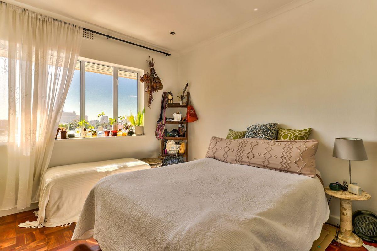 A bright bedroom featuring classic parquet flooring and a large window that allows for ample natural light.