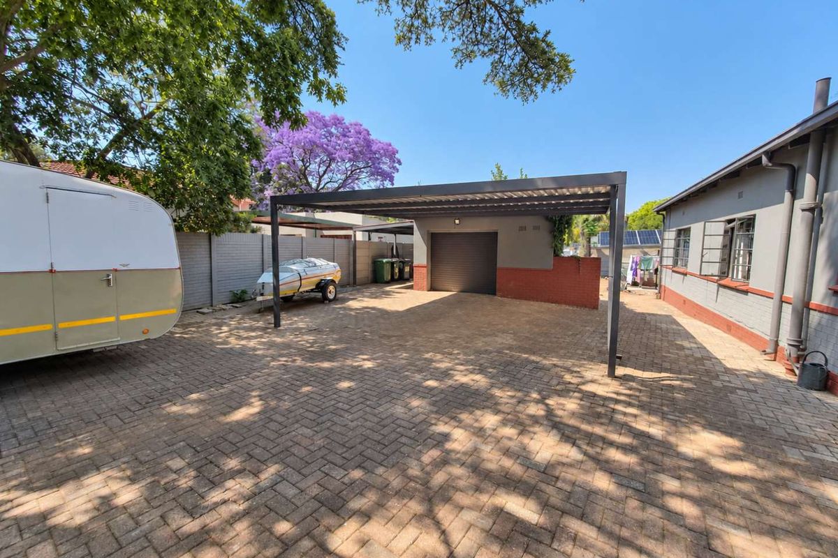 A spacious paved rear courtyard featuring a modern carport, single garage, and secure boundary walling.