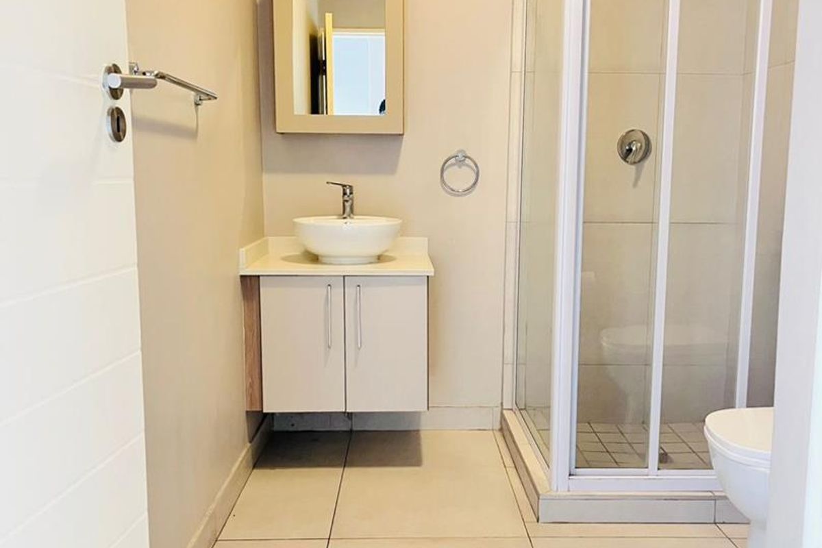A clean and functional bathroom featuring a modern vanity with a vessel sink, a glass-enclosed shower, and neutral floor tiling.