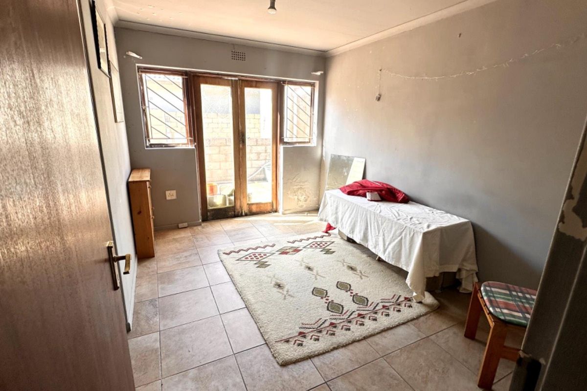 A bedroom featuring tiled flooring and double glass doors leading to an outdoor area, with visible wear on the wall finishes.