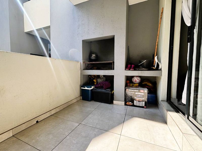 A covered balcony featuring a built-in braai area and tiled flooring, providing a functional outdoor space for relaxation and entertaining.