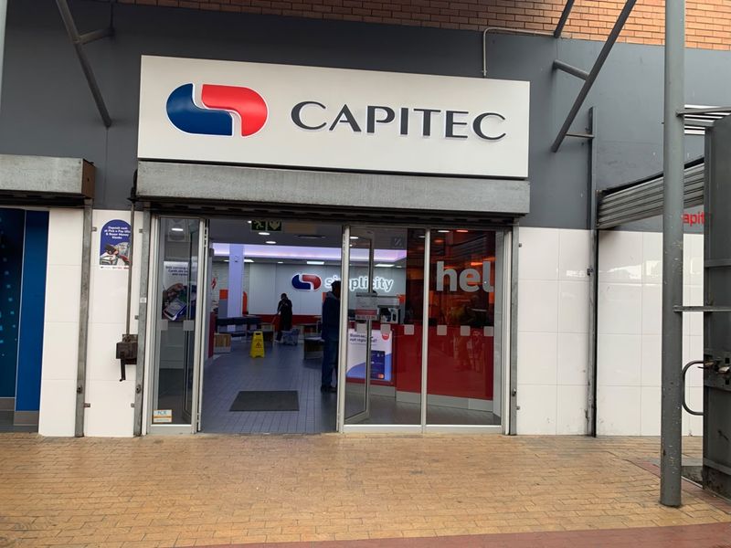 Front entrance of a retail bank branch featuring glass sliding doors, branded signage, and a tiled exterior facade.