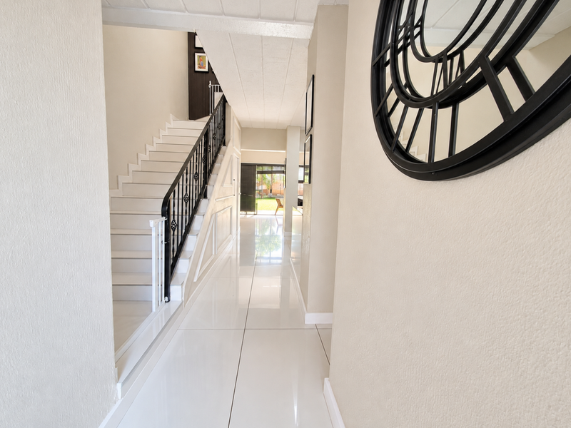 A bright, spacious hallway featuring polished white floor tiles, a modern staircase with a wrought iron balustrade, and clean neutral wall finishes.