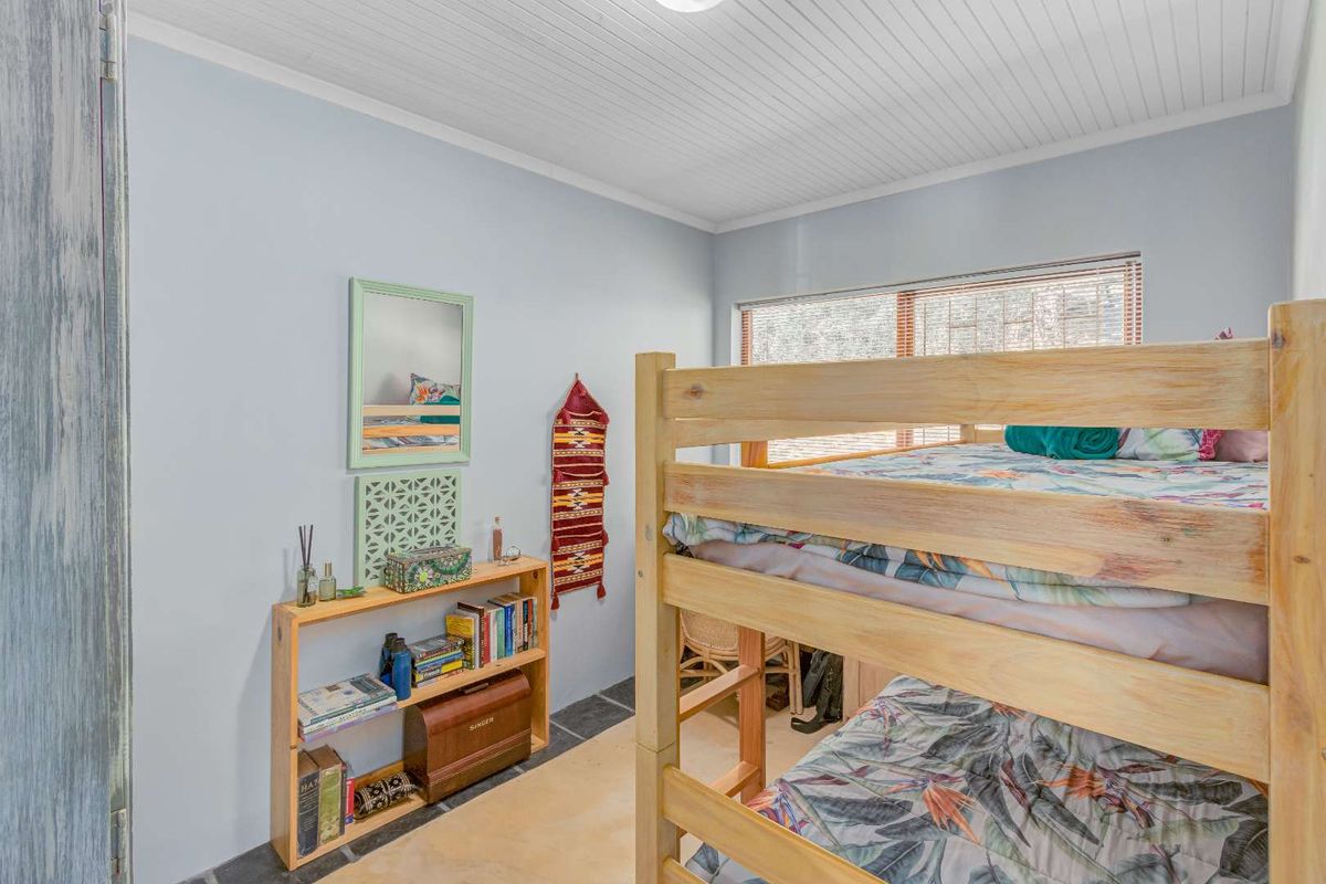 A bedroom featuring a tongue-and-groove ceiling, tiled flooring, and a large window with fitted blinds.
