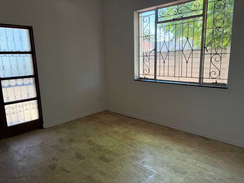 An empty bedroom featuring tiled flooring, a timber frame door, and windows fitted with security bars.