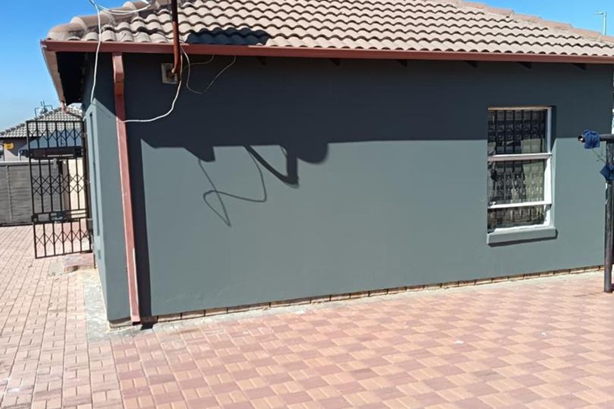 Rear exterior view of the property featuring a tiled roof, paved patio area, and security bars on the window.