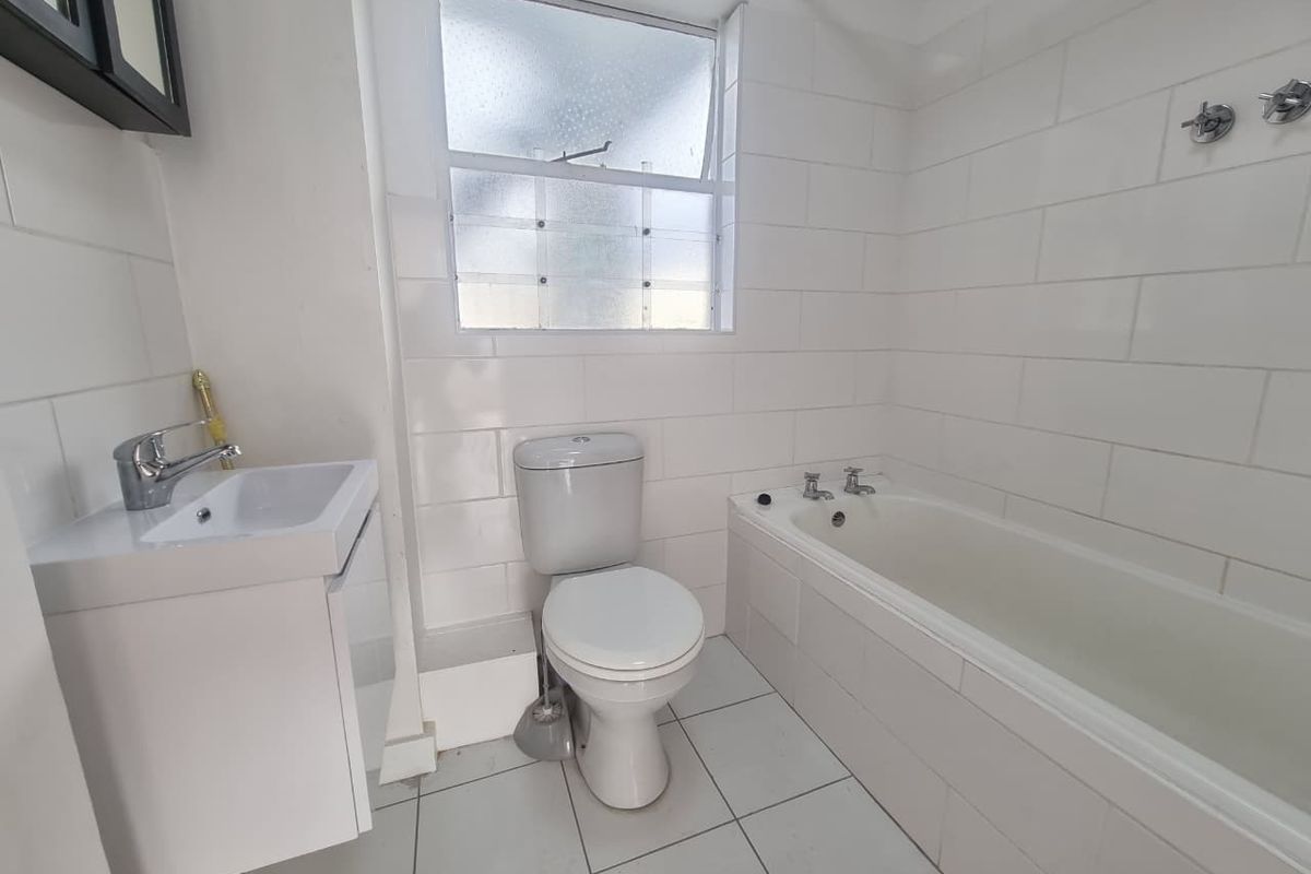 A functional bathroom featuring white wall tiling, a built-in bathtub, a modern vanity basin, and a standard toilet.