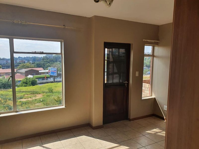 A bright, empty living area featuring tiled flooring, large windows with natural light, and direct access to an exterior space.