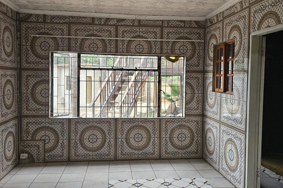 An interior room featuring extensive wall tiling, tiled flooring, and a window with security bars, offering a blank canvas for renovation.
