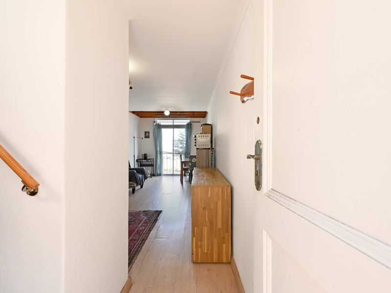 Entryway leading into an open-plan living area with timber ceiling beams, laminate flooring, and access to a balcony through a sliding glass door.