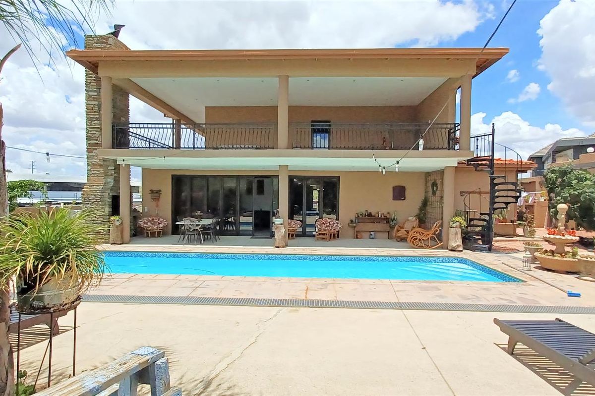 Rear view of a two-story house featuring a swimming pool, covered patio, balcony with metal railings, and a spiral staircase.