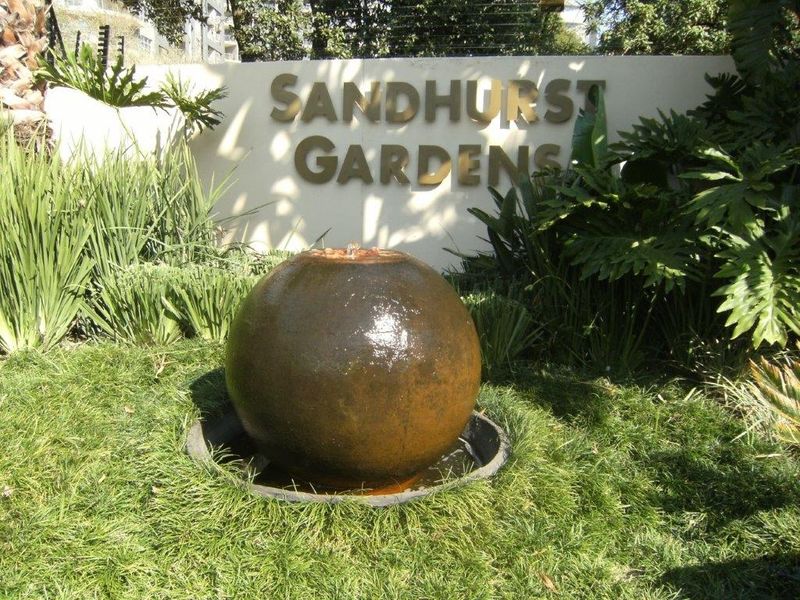 The entrance to Sandhurst Gardens featuring a decorative spherical water fountain set within a well-maintained landscaped garden area.