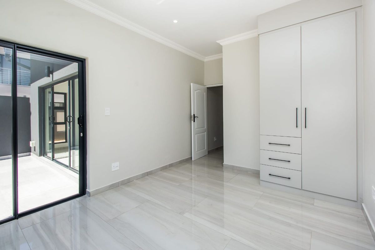A bright, modern bedroom featuring neutral tiled flooring, built-in cabinetry, and sliding glass doors providing direct access to an outdoor area.