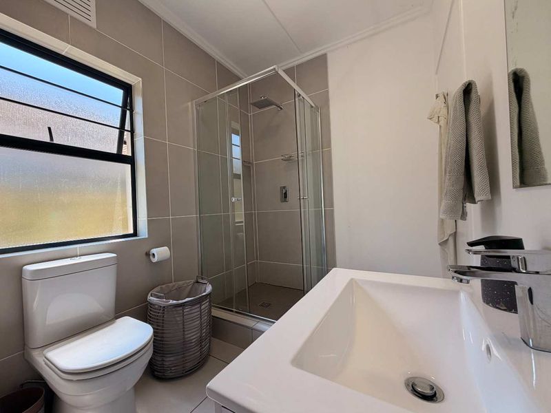 A modern, well-maintained bathroom featuring a glass-enclosed shower, contemporary vanity basin, and neutral wall tiling.