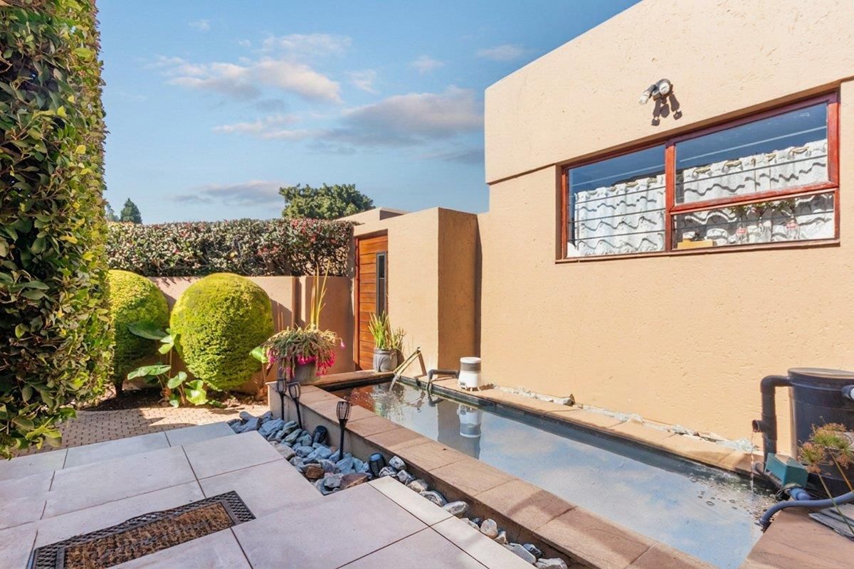 A well-maintained rear courtyard featuring a built-in water feature, paved patio area, and secure boundary walling.