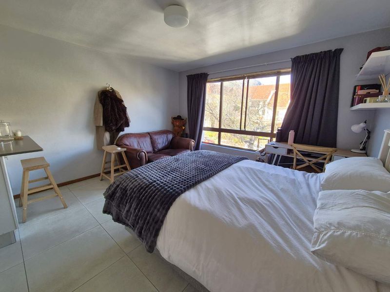 A functional bedroom featuring tiled flooring, a large window providing natural light, and built-in shelving, offering a comfortable living space.