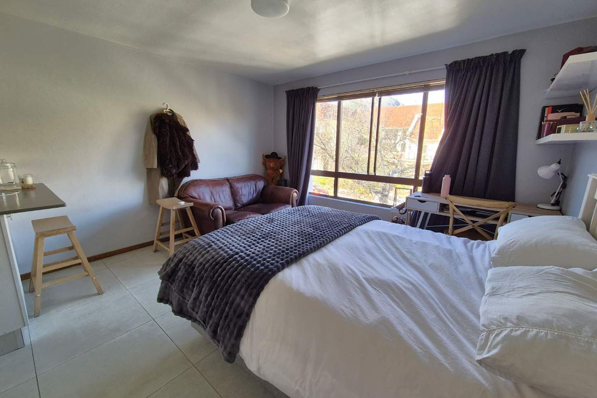 A functional bedroom featuring tiled flooring, a large window providing natural light, and built-in shelving, offering a comfortable living space.