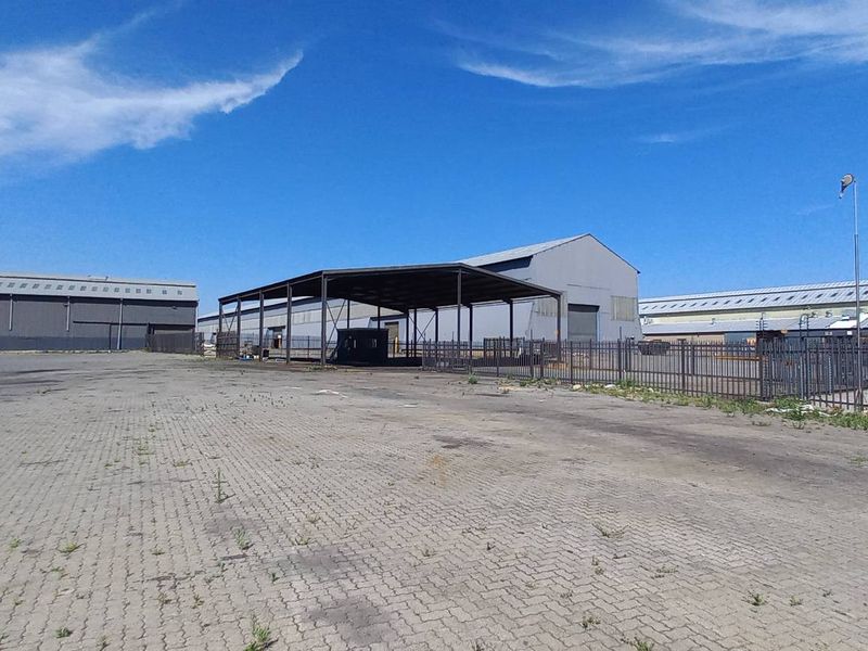 Spacious industrial yard featuring paved surfaces, a large steel-framed canopy, and secure perimeter fencing, suitable for logistics or storage operations.