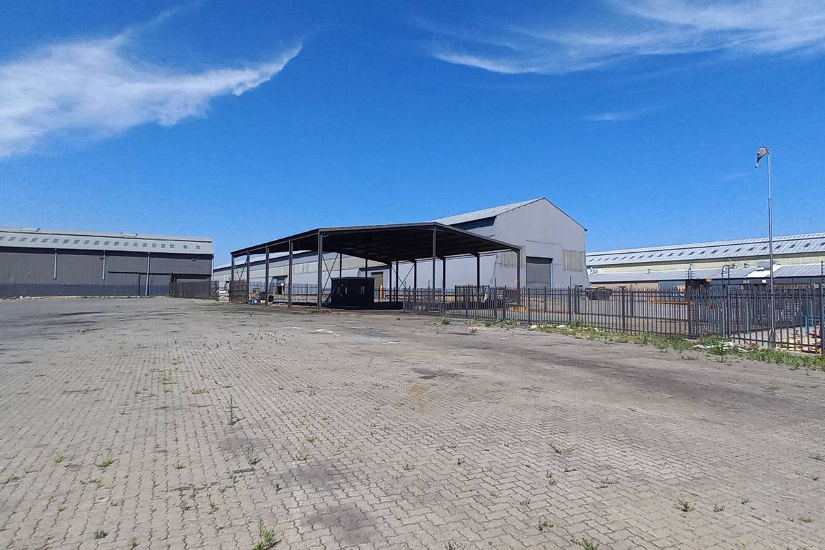 Spacious industrial yard featuring paved surfaces, a large steel-framed canopy, and secure perimeter fencing, suitable for logistics or storage operations.