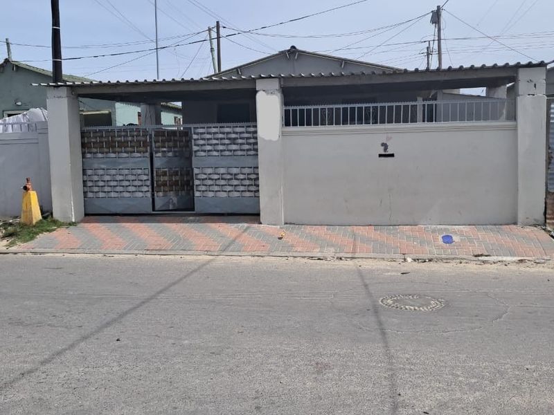 Front exterior view of a residential property featuring a perimeter wall, metal security gate, and paved driveway area.